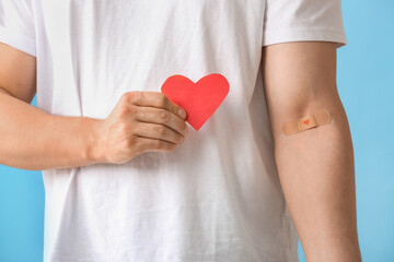 Blood donor with applied medical patch and paper heart on blue background