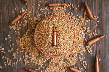 Wheat grains are spread across a wooden table, interspersed with several metal bullet shells. The...
