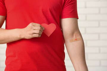 Blood donor with applied medical patch and paper heart in clinic