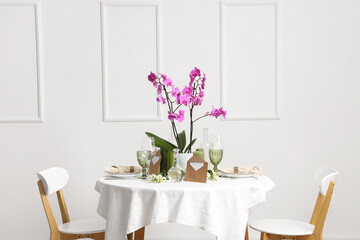 Beautiful table setting with orchid flower for wedding celebration near light wall