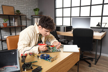Male technician with soldering iron repairing computer at table in service center