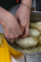 Women cook cabbage rolls while standing at the table and put them in a pot.