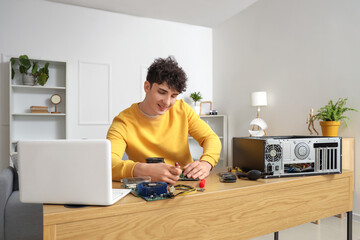 Young technician with screwdriver repairing computer at table in service center