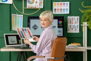 Young female graphic designer working with color palette at table in office
