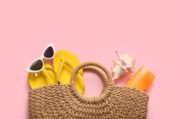 Wicker bag with beach accessories and seashell on pink background
