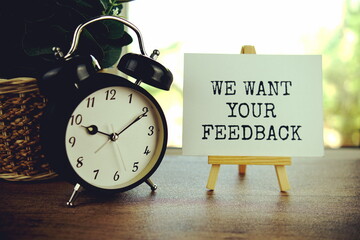 We Want Your Feedback text message on paper card with wooden easel and alarm clock