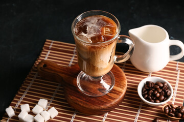 Glass cup of iced latte and bowl with coffee beans on black background