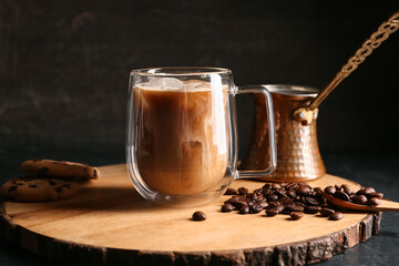 Glass cup of iced latte with coffee beans and cezve on black background