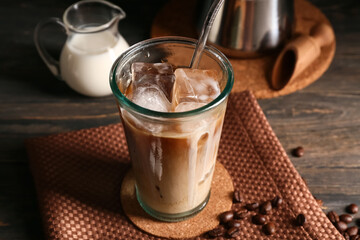 Glass of iced latte with coffee beans and jug of milk on wooden background