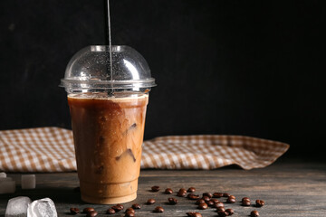 Plastic cup of iced latte and coffee beans on wooden table