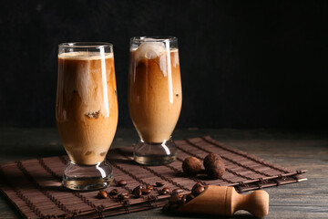 Glasses of iced latte with sweet candies and coffee beans on wooden table