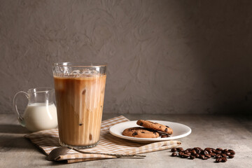 Glass of iced latte and plate with sweet cookies on grey background
