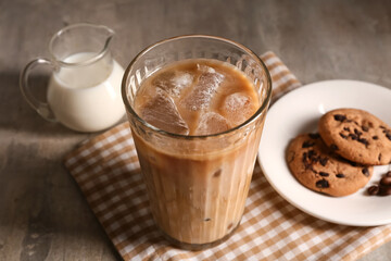 Glass of iced latte and plate with sweet cookies on grey background
