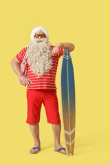 Santa Claus with beach bag and surfboard on yellow background. Christmas in July