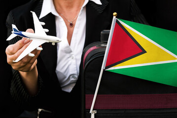 business woman holds toy plane travel bag and flag of Guyana
