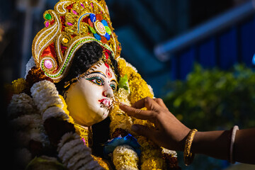 Devotee performing baran ritual during Saraswati Puja, offering prayers and touching the idol with...