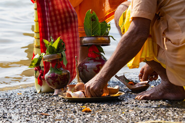 Hindu puja rituals being performed by priest with copper vessels, mango leaves and red sindur and other religious items.