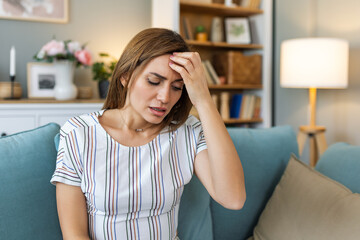 Headache. Close-up photo of a young woman, who is sitting on a sofa , touching her head while...