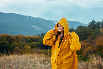 A woman with a yellow raincoat standing in a vast field with majestic mountains in the background, representing beauty and nature exploration