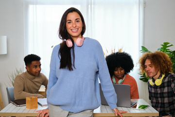 Young Caucasian woman smiling and looking at camera with her college mates studying in the background.