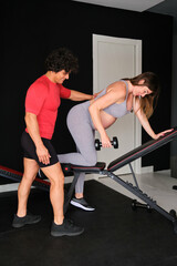 Pregnant woman working out with a dumbbell supervised by a male personal trainer at the gym.