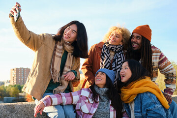 Multiracial young people taking selfie pic with smart mobile phone device. Photo of happy friends smiling at camera. Life style concept with guys and girls hanging out on autumn day.