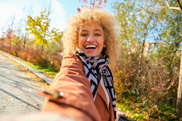 Young Brazilian woman smiling and taking a selfie in a park in autumn.