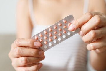 Contraceptive means: Woman hand holding contraceptive pills and condom sitting on sofa background. Protection, safe sex. Contraception, concept birth control. Copy space