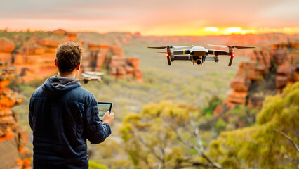 A person controls a flying drone with a remote control in a scenic canyon at sunset, capturing...