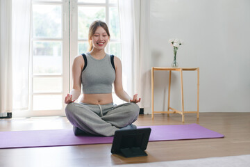 Young Asian woman at home doing yoga in front of open laptop, repeating instructions by...