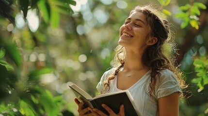 Young woman enjoying nature and the pleasure of reading a book outdoors amid lush greenery, smiling and feeling relaxed and happy.