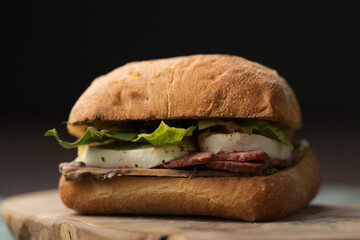 Roast beef and mozzarella sandwich with ciabatta bun on olive board