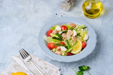 Salad with asparagus, canned tuna, tomatoes and mozzarella cheese on a ceramic plate on a light concrete background. Healthy eating, lifestyle.
