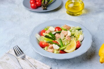 Salad with asparagus, canned tuna, tomatoes and mozzarella cheese on a ceramic plate on a light concrete background. Healthy eating, lifestyle.