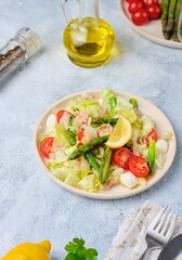 Salad with asparagus, canned tuna, tomatoes and mozzarella cheese on a ceramic plate on a light concrete background. Healthy eating, lifestyle.