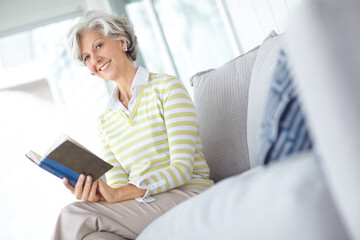 Senior woman, book and portrait on sofa in home with smile, literature or relax with poetry in...