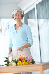 Senior woman, vase and bouquet in house with portrait, smile and natural floral decoration in morning. Mature person, happy and style with flowers, hobby and glass container in home for retirement