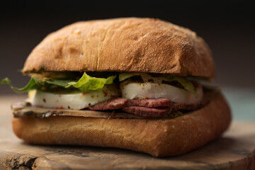 Roast beef and mozzarella sandwich with ciabatta bun on olive board