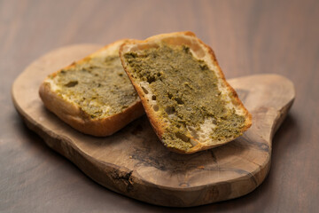 Ciabatta bun sliced in halves with pesto sauce on olive board