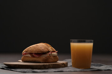 Sandwich with bresaola, mozzarella and pest on olive board with orange juice