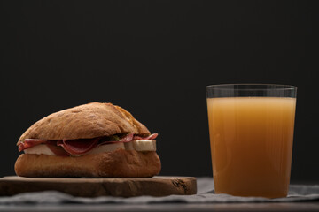 Sandwich with bresaola, mozzarella and pest on olive board with orange juice