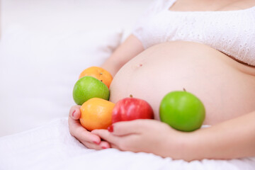 pregnant woman sitting on sofa with apple, orange,  in her hands close up selective focus.