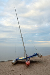 Catamaran with mast on lake shore.
