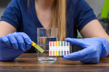 Kobieta chemik sprawdza odczyn kwasowości wody sieciowej papierkiem lakmusowym, alkalizacja wody pitnej 