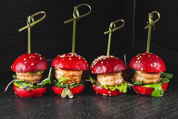 A row of four mini burgers with red buns, likely dyed with beetroot juice, skewered with...