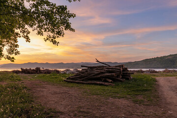 A tranquil scene captures the warm hues of a sunset over a lake, with a pile of logs and a solitary...