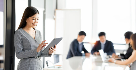 Portrait of confident businesswoman with colleagues in boardroom. Using digital tablet during a meeting.