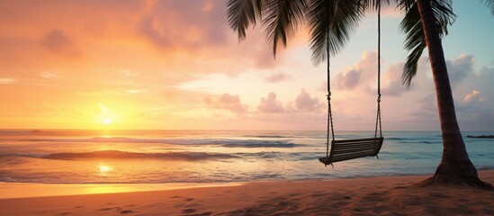 A swing is attached to a palm tree on a sandy tropical beach by the ocean during sunset creating a tranquil scene with a perfect copy space image