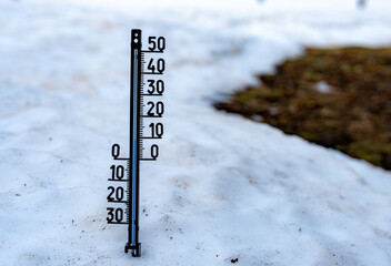 Thermometer with celsius scale stuck in melting snow as climate change concept