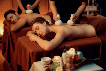 Hot herbal ball spa massage body treatment, masseur gently compresses herb bag on couple customer...